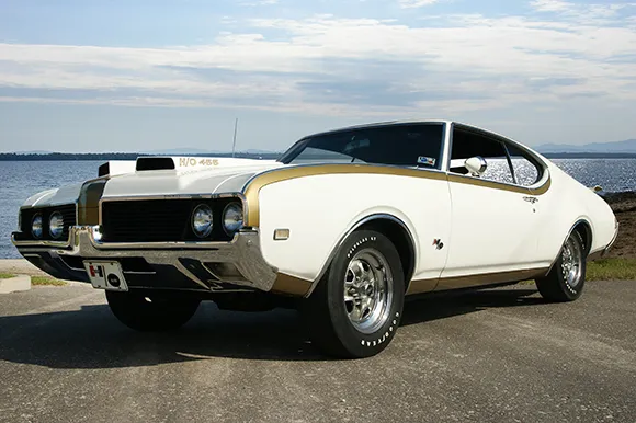 A 1969 Oldsmobile Cutlass Hurst Olds muscle car in front of a lake.