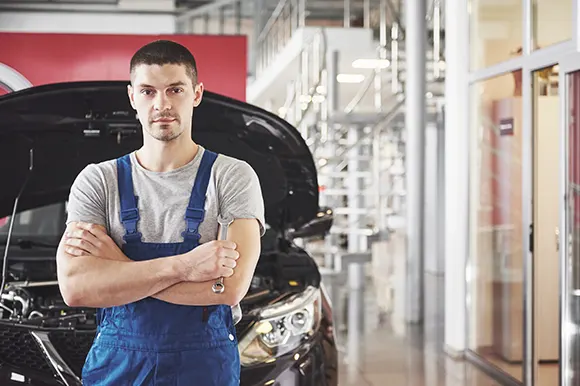 A car mechanic posing while holding a wrench inside a car garage