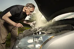An middle-aged man trying to repair his overheating car engine